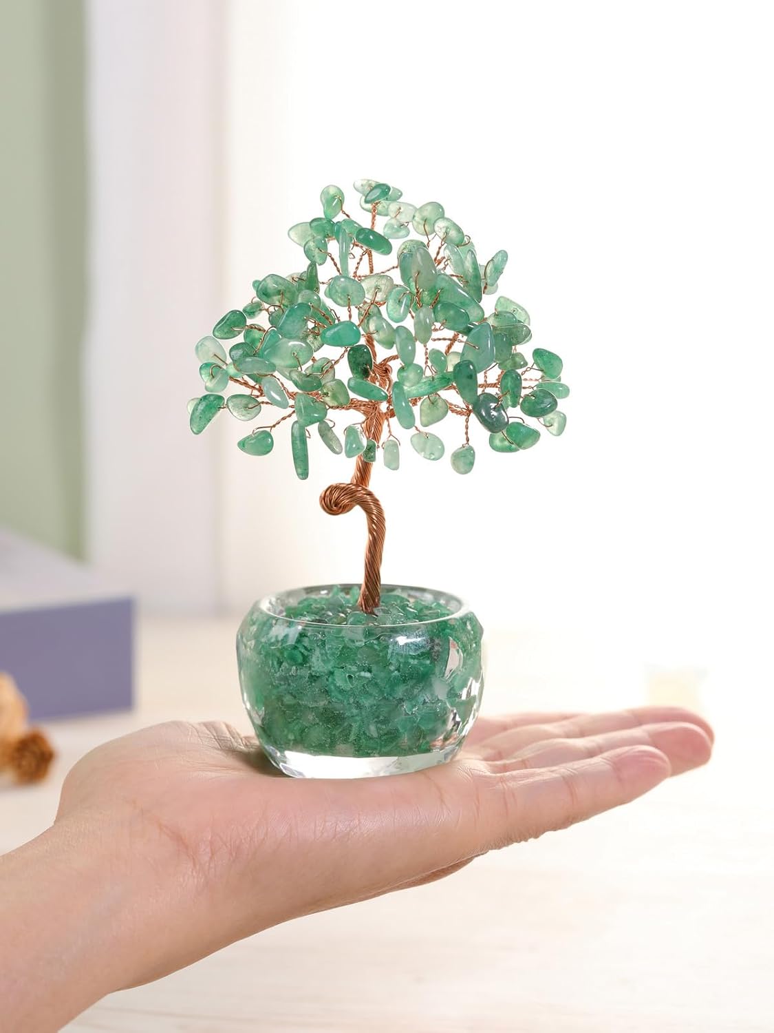 Small green aventurine crystal money tree with a copper wire trunk, planted in a glass pot of aventurine chips, shown palm-sized in a hand