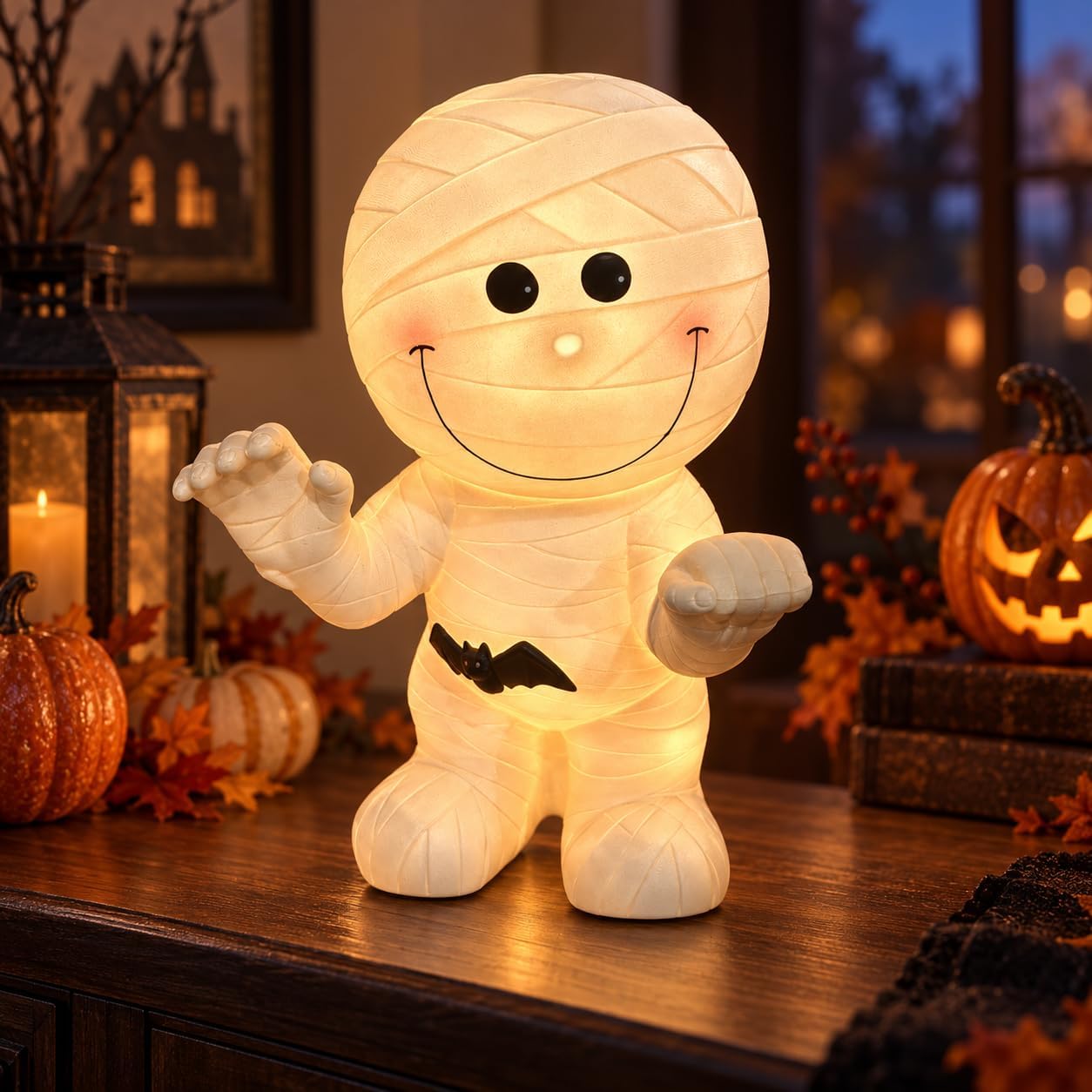 Smiling resin mummy lamp with warm glow, rosy cheeks, and a little bat charm, standing with arms raised