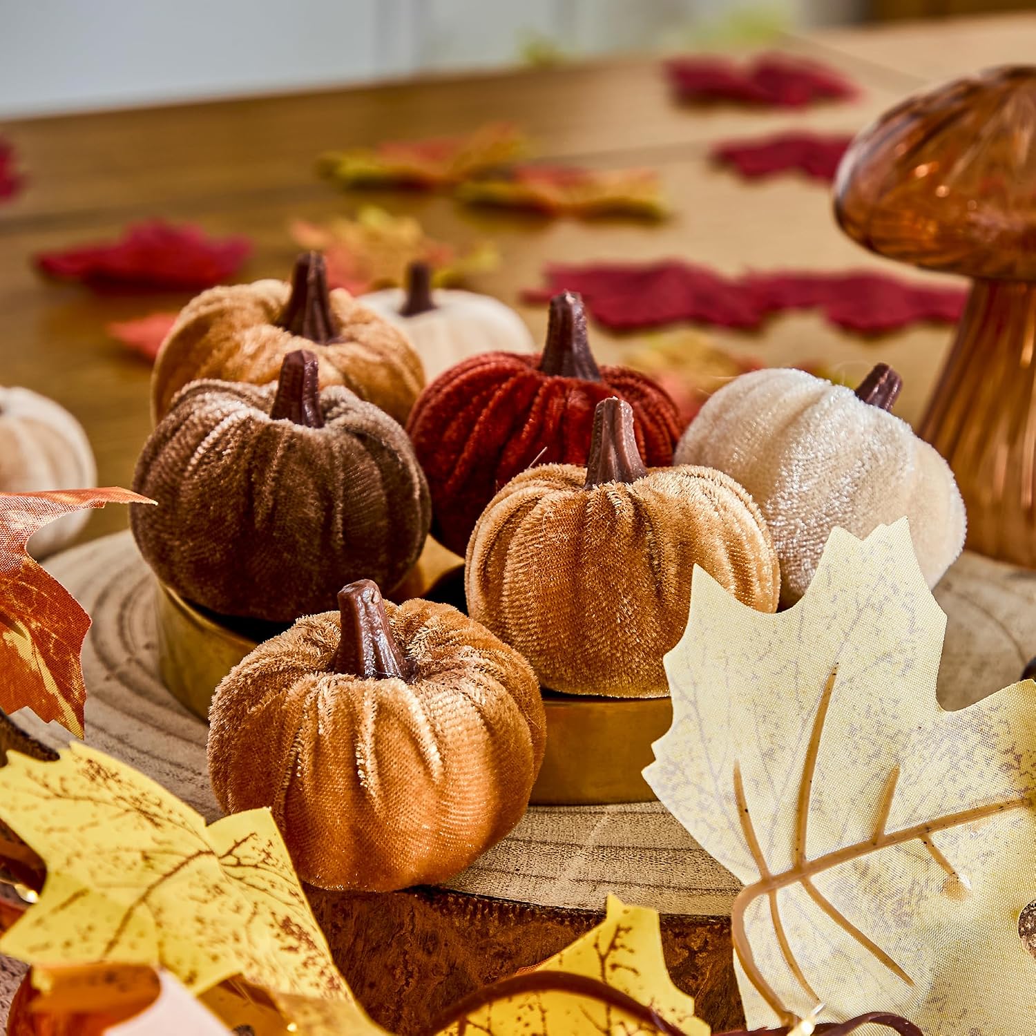 Set of velvet fabric mini pumpkins in mixed autumn colours — rust, brown, cream and gold — styled with fall leaves on a wooden table