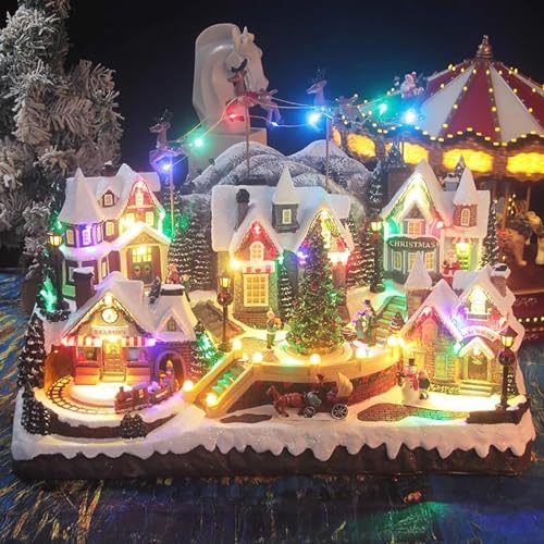 Large animated Christmas village display lit in multicoloured lights, with snowy houses, a lit Christmas tree, a carousel, a little train, and Santa's sleigh and reindeer flying over a snowy mountain