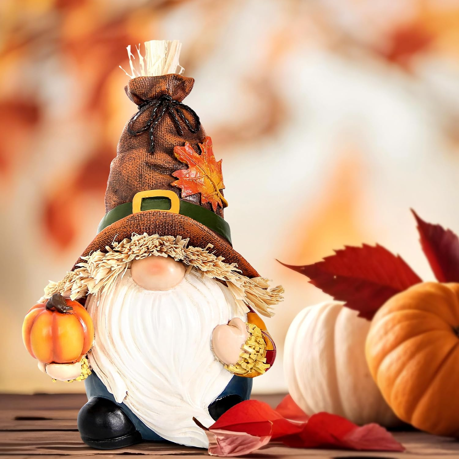 Resin autumn gnome ornament in a burlap hat cradling a pumpkin amid autumn leaves