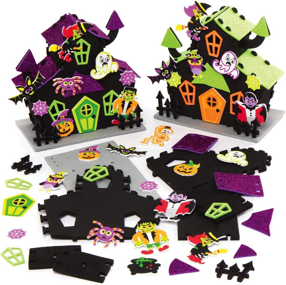 Two finished foam haunted house craft models, one with purple glitter roofs and one with green, decorated with stick-on witches, ghosts, bats, spiders, owls and pumpkins, with the flat foam pieces and stickers laid out in front