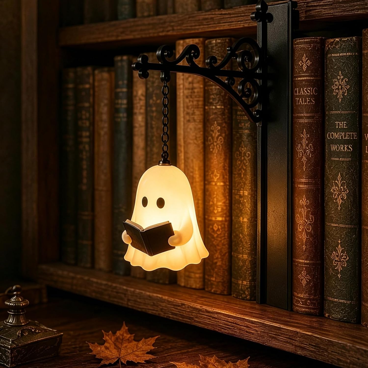 Little glowing ghost lamp reading a tiny book, hanging on a chain from a black wrought-iron bracket that slots between old leather-bound books on a shelf