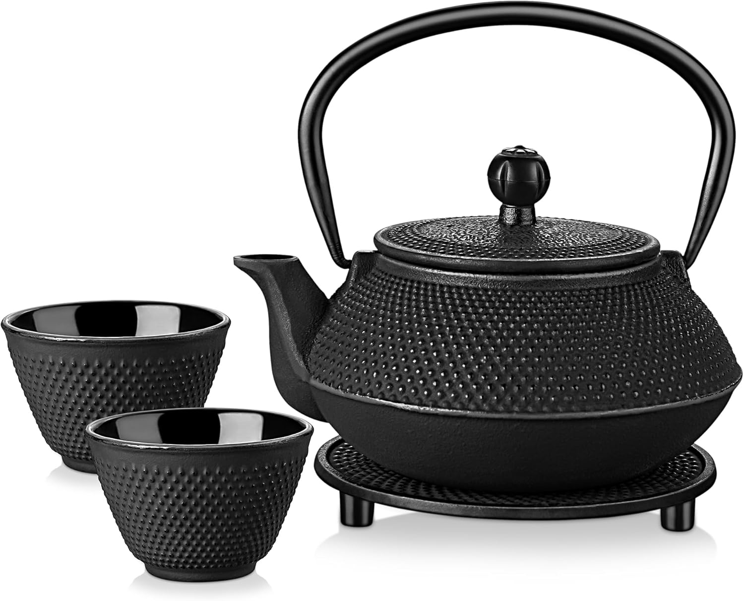 Black cast iron Japanese tetsubin teapot with a hobnail pattern, on a trivet with two matching cast iron cups